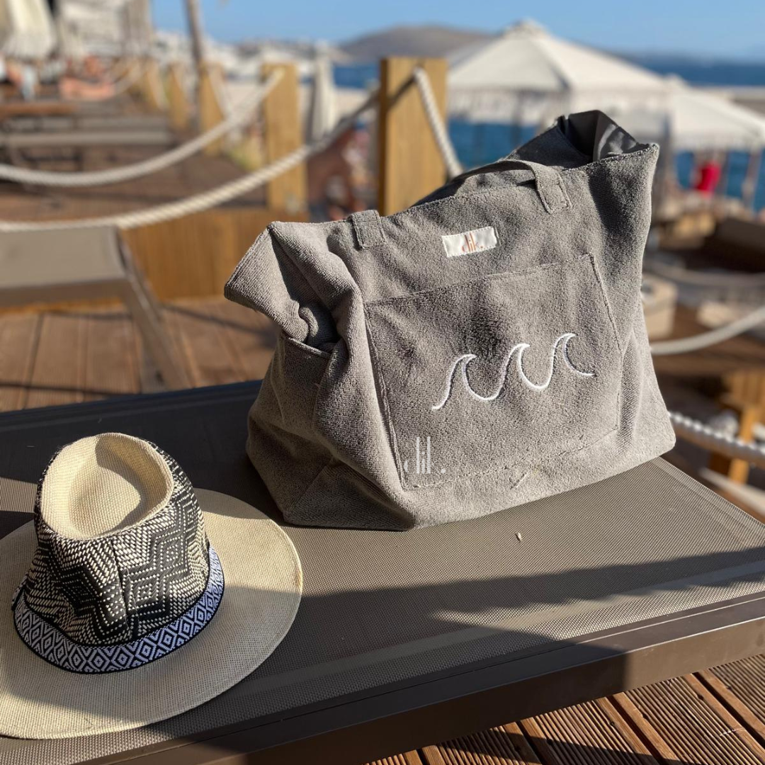 Gray bag with wave design and straw hat on a wooden surface with beach background